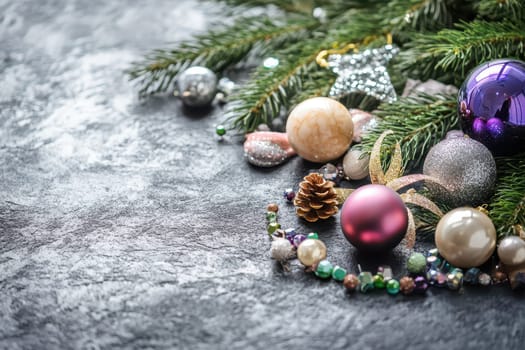 A collection of sparkling Christmas ornaments pine branches and a pinecone arranged on a dark textured surface for the holiday season.