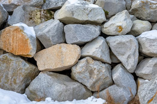 A collection of various rocks and stones resting atop each other in a snowy environment showcasing natures textures and colors.