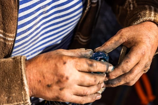 Dirty and calloused hands of a mechanic assembling compressed coil spring during DIY car repairs. Closeup.