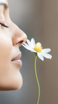 A serene woman enjoys the fragrance of a daisy, appreciating the beauty of nature in a close up shot.