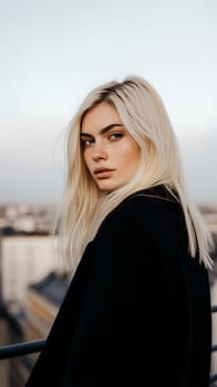 A woman with long blonde hair gazes thoughtfully from a rooftop, cityscape softly blurred in the background.