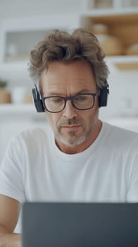 A mature man wearing glasses and headphones concentrates on his work, deeply engaged in a modern workspace.