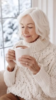An elderly woman in a cozy sweater savors a hot drink by the window, embracing the warmth of winter indoors.