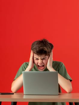Teenager expressing frustration in front of a laptop with a bright red background, copy space.