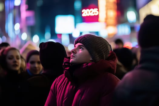 A crowd gathers to celebrate New Year in a vibrant city. A young man looks upward captivated by colorful lights and the coming year.