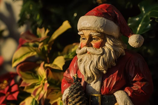 A detailed Santa Claus figurine holding a pine cone stands among colorful holiday plants creating a warm festive atmosphere.