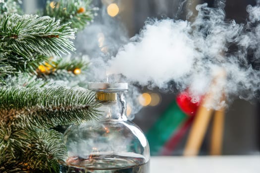 A glass container emits smoke and sits next to a decorated Christmas tree creating a cozy holiday atmosphere indoors.