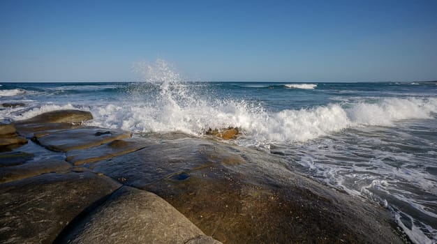 White foaming water splashes as surf waves break over large rock platform on the foreshore of the rocky headland at Point Cartwright, Kawana, Queensland