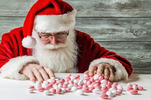 Santa is focused on counting an assortment of colorful candies on a white table embodying the festive spirit of the holiday season.