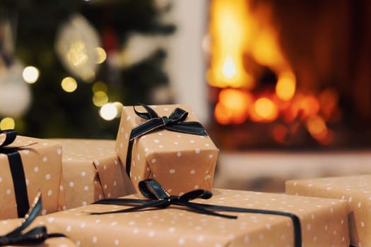 Wrapped Christmas gifts with black ribbon bows against burning fireplace and christmas tree decorated with lights. Warm winter family atmosphere, Magical Holiday time