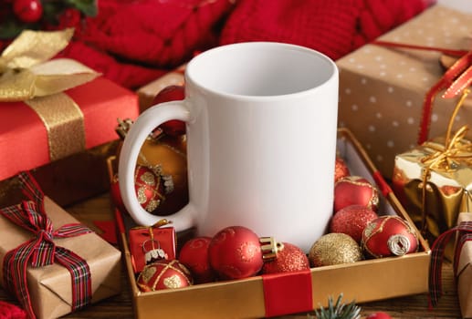 White blank coffee mug near white knitted sweater, wooden Christmas decor and lights, copy space. Winter atmospheric mock up in rustic or scandinavian style