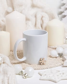 White blank coffee mug near candles, white knitted sweater and Christmas decor, copy space. Winter atmospheric mockup in rustic or scandinavian style