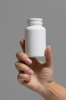 Female hand holding a white plastic pill bottle closeup against grey background. Packaging mockup for your pills or capsules herbal supplement