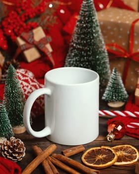 White ceramic coffee mug near Christmas decor, presents, trees, spices and red knitted sweater on wooden table closeup, copy space. Winter atmospheric mock up, holiday time