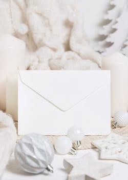 Blank white envelope near candles, white knitted sweater and Christmas decor, copy space. Winter atmospheric mockup, family greeting in rustic or scandinavian style