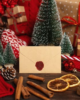 Beige sealed envelope near Christmas decor, trees and red knitted sweater on wooden table closeup, place for text. Winter mock up for greeting card or invitation