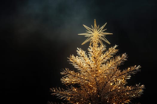 Golden christmas tree with star decoration shining brightly against a dark background, creating a festive atmosphere