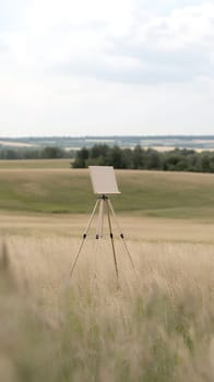 A blank canvas on an easel stands in the middle of a vast, grassy field under a cloudy sky, inviting creativity.