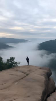 A solitary figure stands atop a cliff, overlooking a foggy valley, embodying solitude and reflection in nature.