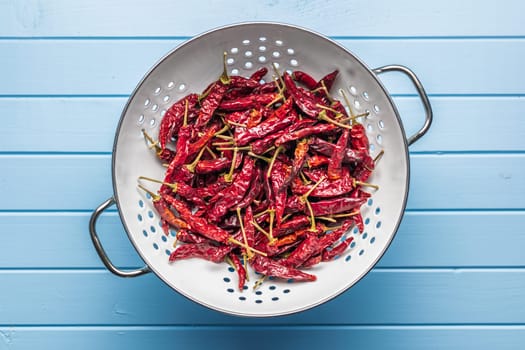 Dried red chili peppers in colander on a blue table. Top view.