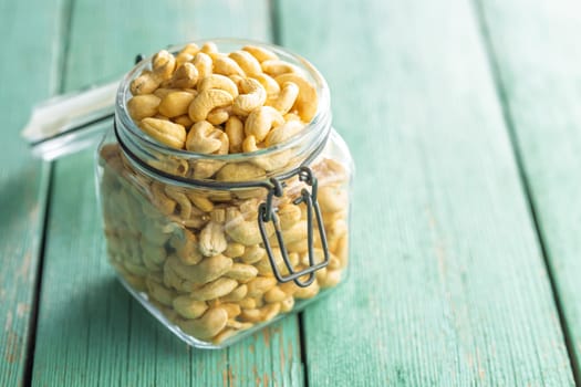 Roasted cashew nuts in jar on a green wooden table.