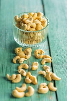 Roasted cashew nuts in bowl on a green wooden table.
