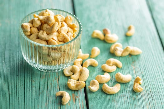Roasted cashew nuts in bowl on a green wooden table.