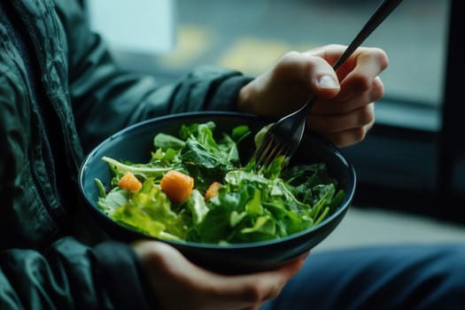Hands holding a bowl of fresh green salad with croutons and using a fork