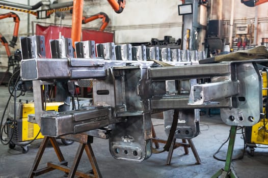 A large metal frame undergoing assembly in an industrial workshop, surrounded by heavy machinery and equipment for fabrication.