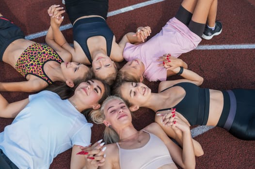 Group of tired and happy fit young girls resting on floor at stadium