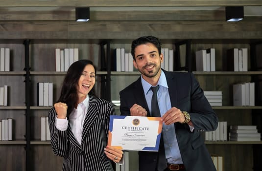 Happiness Caucasian businesswoman and Asian businessman showing fist pump while holding success business certificate  in a modern office. Achievement career wealth business concept.