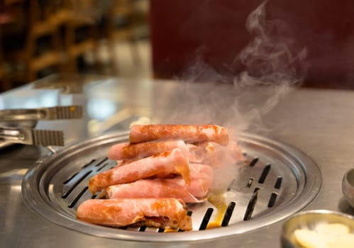 Sizzling marinated pork slices being grilled on charcoal in a Korean restaurant. Korean or Japanese BBQ style cuisine.