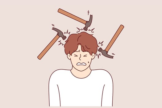 Headache and migraine torment man making painful grimace, standing among hammers. Problem of headaches caused by stress and noisy neighbors necessitates taking antibiotics and painkillers