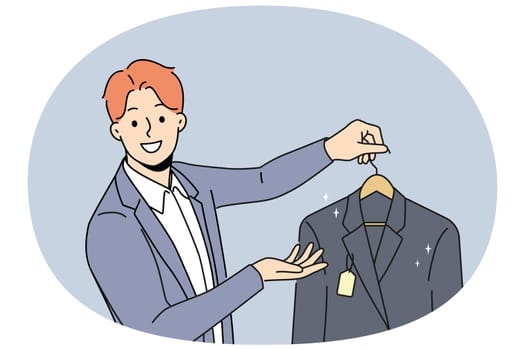 Man holds new jacket with tag offering to buy business clothes for managers or clerks. Guy works as salesman or dry cleaning employee and looks at screen with smile, giving client jacket on hanger
