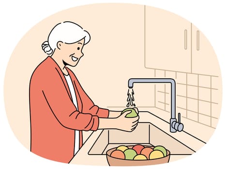 Elderly woman washes fruits in sink, standing in kitchen and observing rules of hygiene to avoid infection. Grandmother washes vegetables before preparing dinner, following recommendations of doctors