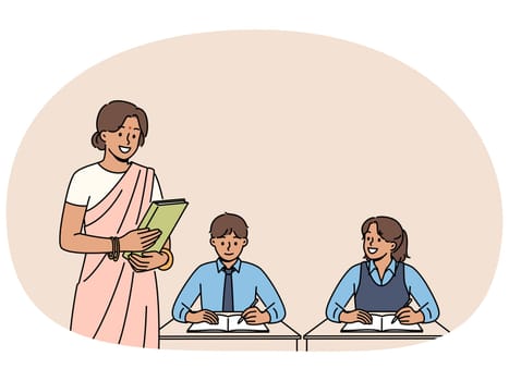Indian woman teacher works in primary school, standing near children sitting at desks in classroom. Girl teacher from india, makes career in education and gives kids new knowledge.