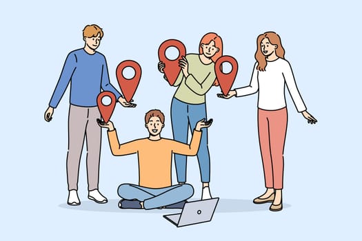 Team of students uses online communication on network, standing near laptop and holding red geotags in hands. Online communication technology for educational or professional purposes