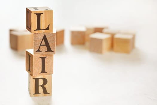Four wooden cubes arranged in stack with text LAIR (meaning Listen, Acknowledge, Identify, Reversal) on them, space for text / image at down right corner