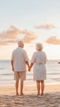 An elderly couple holds hands on the beach at sunset, symbolizing love, connection, and companionship.
