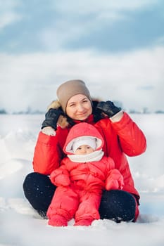 Happy mother and baby are sitting on the snow and enjoying a beautiful winter day