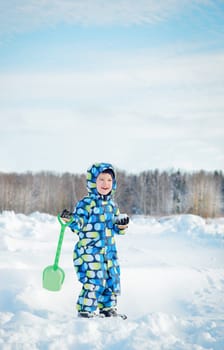 Happy child holding snowball and shovel, enjoying winter games in snowy landscape