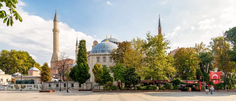 Istanbul, Turkey - August 30 2022: Few visitors stroll through lush gardens in front of Hagia Sophia Grand Mosque. The historic architecture is set against clear blue sky, creating serene atmosphere