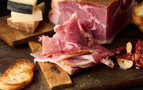 A piece of prosciutto, slices of ciabatta and cheese on a wooden board
