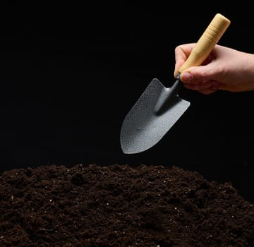 A woman's hand holds a small garden trowel over a pile of damp, loose soil, the beginning of farming