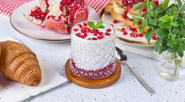 Glass of yogurt with chia seeds, pomegranate seeds and baked croissants on table