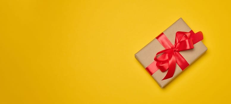 Gift box with red satin ribbon and bow on a yellow background. Holiday background, Copy space