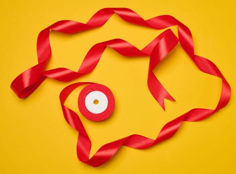Spool of red silk ribbon on yellow background, top view