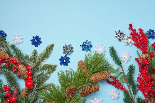 Decorative Christmas branch with red berries and pine cones on a blue background, top view. Copy space