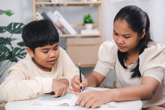 Teacher or sister helping boy writing lesson and learning to write  Female tutor helping little elementary school boy with homework during individual lesson at home  Education home school concept.
