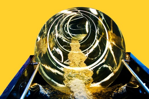 Slide in the water park. Abstract closeup at the end of an endless large round gold coloured water slide with flowing water on yellow background with copy space. Spa.